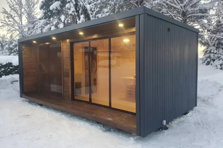 Nowoczesna całoroczna sauna ogrodowa z dużymi przeszkleniami usytuowana w zimowej scenerii.